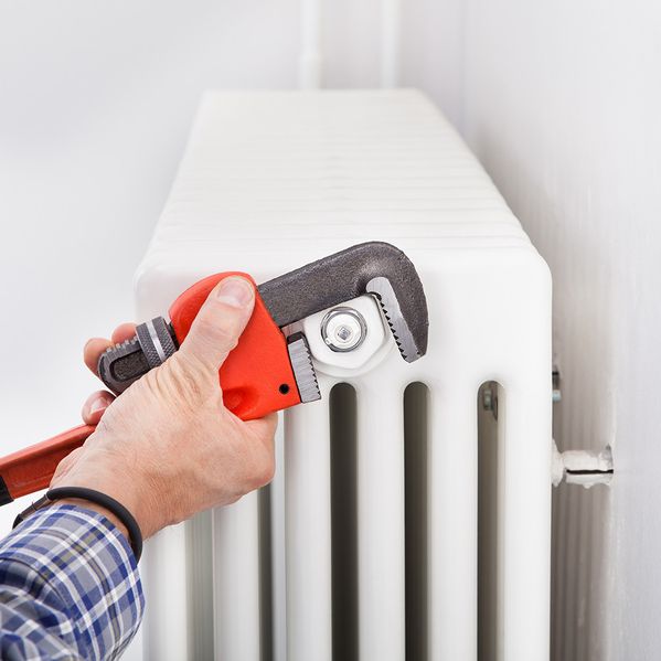 Eine Person, die mit einem Werkzeug eine Heizung repariert.