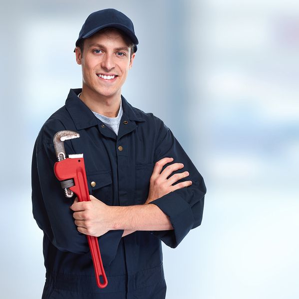 Ein Mann im Blaumann und mit Cap, der ein Werkzeug in der Hand hält und freundlich lächelt.