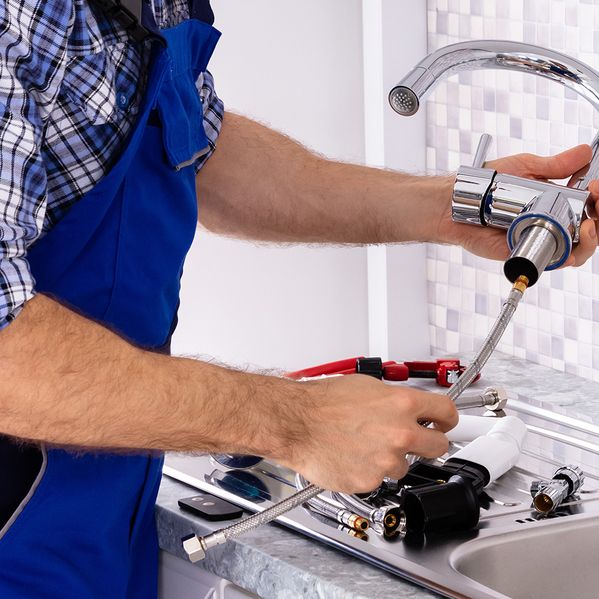 Ein Mann im Blaumann, der einen Wasserhahn wechselt.