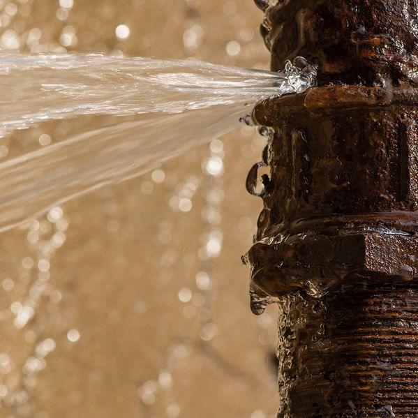 Ein kaputtes Rohr aus der Nähe, aus dem Wasser herausspritzt.