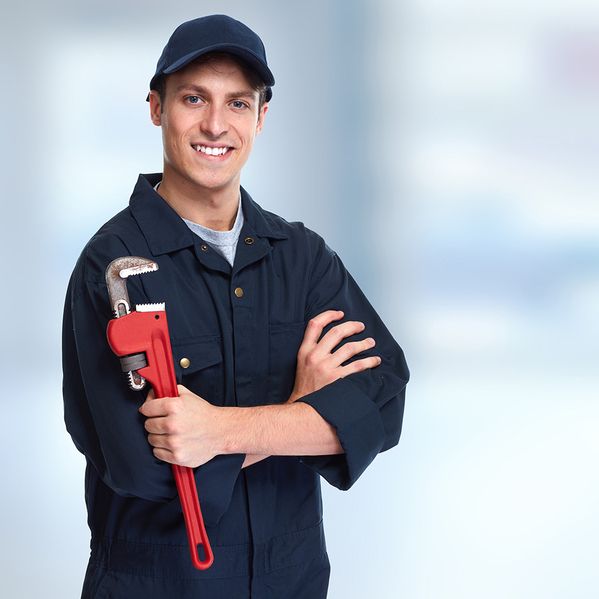 Ein Mann im Blaumann und mit Cap, der ein Werkzeug in der Hand hält und freundlich lächelt.
