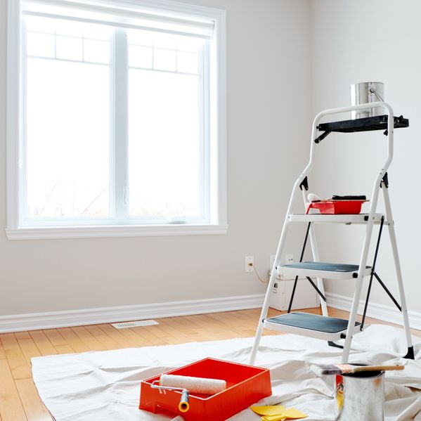 Eine Leiter mit Werkzeug darauf und eine weiße Wand im Hintergrund.