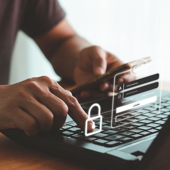 Eine Person mit Handy in der Hand, die ein Passwort in den Computer eingibt.